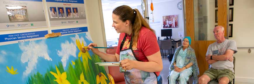 Center Stage Arts in Health member painting sunflowers while two people admire her work.