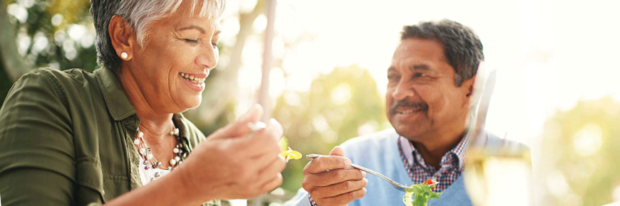 An older male and female sit outside eating salad.