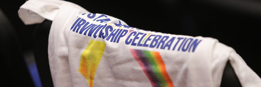 A white short sleeved t-shirt hanging over a chair that says survivorship celebration.
