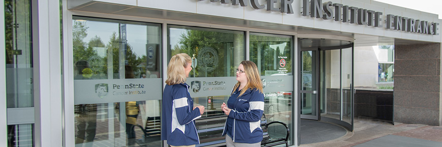 Two females have a conversation at the entrance of the Penn State Cancer Institute