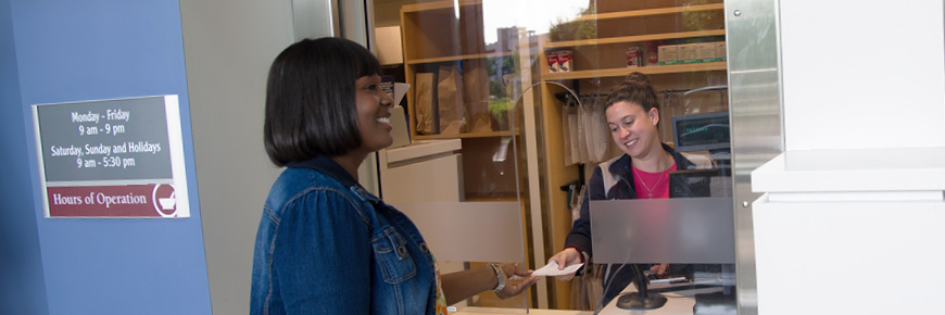 A woman at a Pharmacy window hands a prescription to the pharmacy technician.